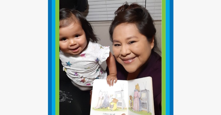 Mother holding up a book next to her young daughter