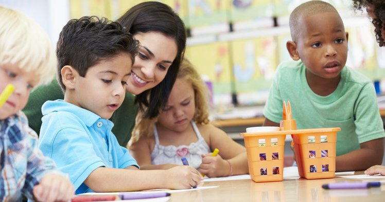 Teacher working with preschool aged boys and a girl in a classroom.