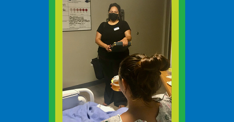 Woman standing in hospital room talking to mother who recently gave birth to a child.