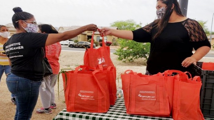 A woman in black t-shirt is handing a bag of produce to another woman.