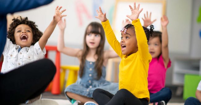 children sitting on floor raising both hands